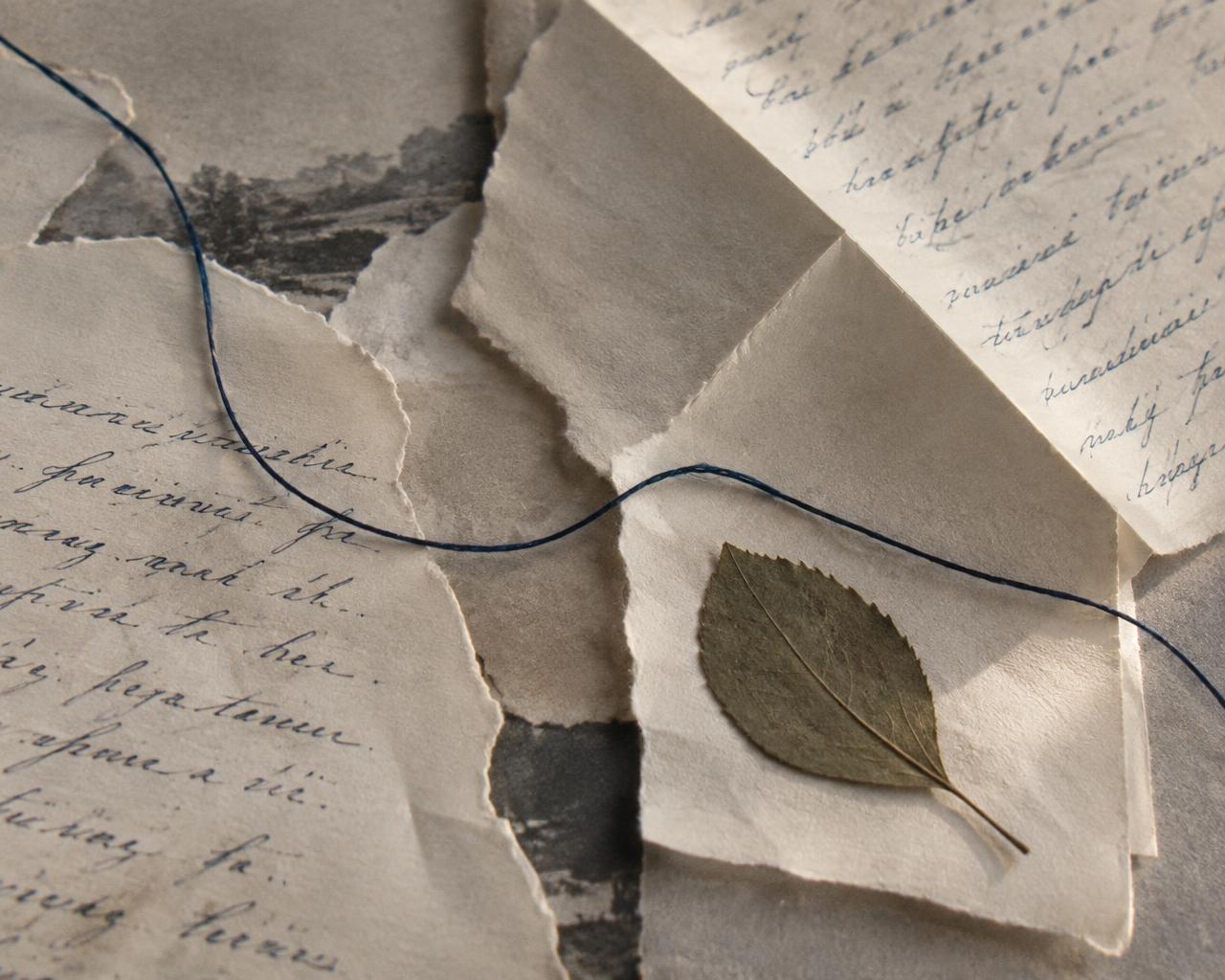 Fragmentos de papel escrito a mano, un pliegue y un hilo azul que los atraviesa.